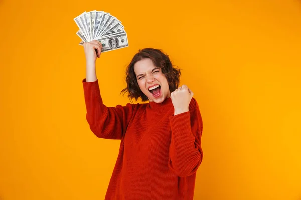 Opgewonden gelukkig jonge mooie vrouw poseren geïsoleerde over gele muur achtergrond aanhouden van geld. — Stockfoto