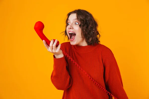 Емоційна молода красива жінка позує ізольовано на жовтому фоні стіни, розмовляючи по телефону . — стокове фото