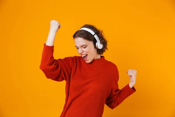 Emocional joven bonita mujer posando aislada sobre fondo amarillo de la pared escuchando música con auriculares . —  Fotos de Stock