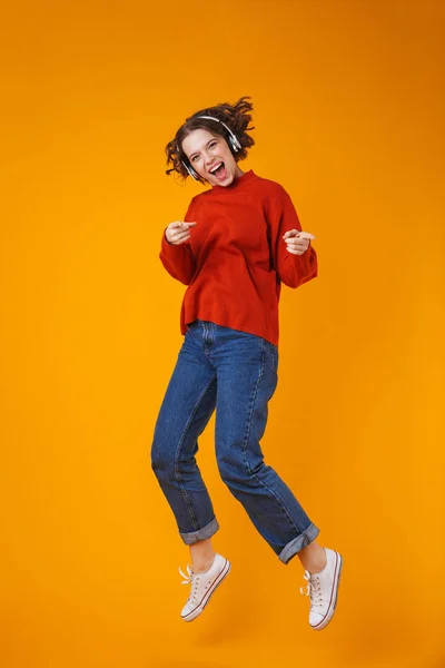 Emocional joven bonita mujer posando aislada sobre fondo amarillo de la pared escuchando música con auriculares . —  Fotos de Stock