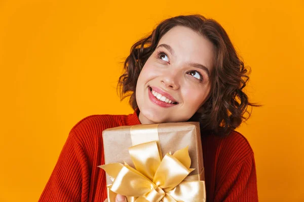 Emocional joven bonita mujer posando aislada sobre fondo amarillo de la pared sosteniendo regalo presente . — Foto de Stock