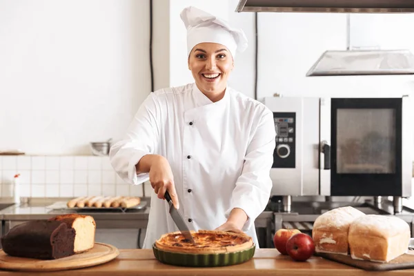 Imagen de la mujer feliz chef vistiendo uniforme blanco sosteniendo manzana pi —  Fotos de Stock