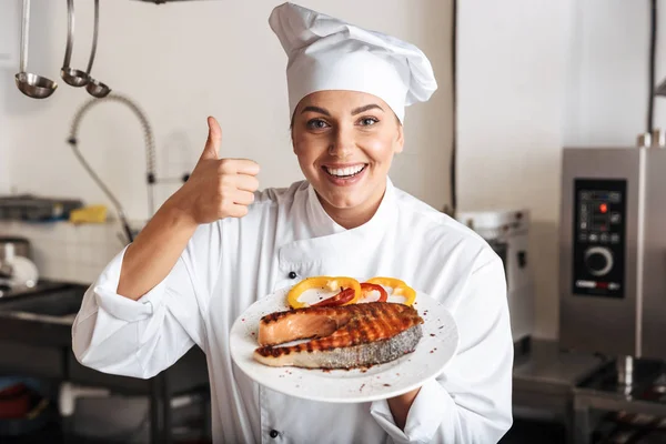 Imagen de mujer positiva chef vistiendo uniforme blanco, sosteniendo plat —  Fotos de Stock