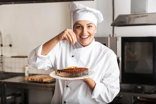 Imagen de la mujer alegre chef vistiendo uniforme blanco, sosteniendo plat —  Fotos de Stock