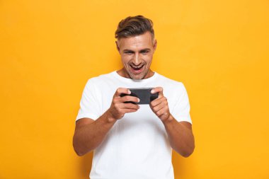 Duygusal adam sarı duvar arka plan üzerinde izole poz oynamak Oyunlar cep telefonu.
