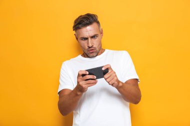 Duygusal adam sarı duvar arka plan üzerinde izole poz oynamak Oyunlar cep telefonu.