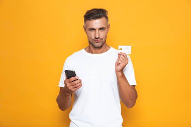 Neşeli adam 30'lu yaşlarda beyaz t-shirt holding cep telefonu görüntüsünü bir