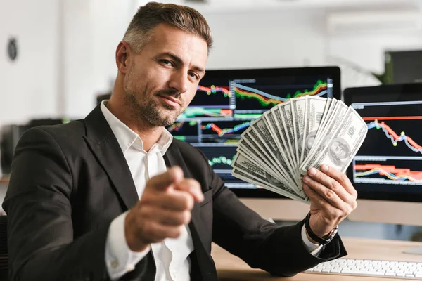 Imagen de empresario satisfecho sosteniendo el ventilador del dinero mientras que trabaja en — Foto de Stock