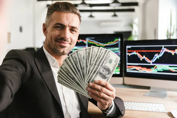 Imagen de un hombre de negocios guapo sosteniendo ventilador de dinero mientras trabajaba en — Foto de Stock