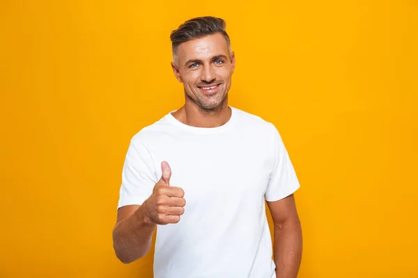 Handsome emotional man posing isolated over yellow wall background showing thumbs up gesture. — Stock Photo, Image