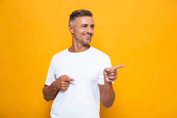 Happy excited man posing isolated over yellow wall background pointing.