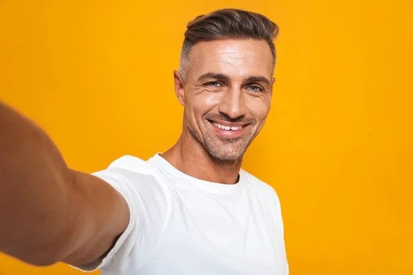 Imagem de homem alegre 30 anos em t-shirt branca sorrindo e tomando auto — Fotografia de Stock