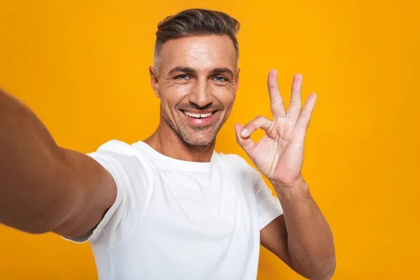 Εικόνα του μελαχρινή άνθρωπος 30s σε λευκό t-shirt χαμογελώντας και λαμβάνοντας se — Φωτογραφία Αρχείου