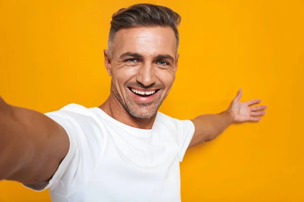 Imagem do homem feliz dos anos 30 na t-shirt branca que sorri e que toma selfi — Fotografia de Stock