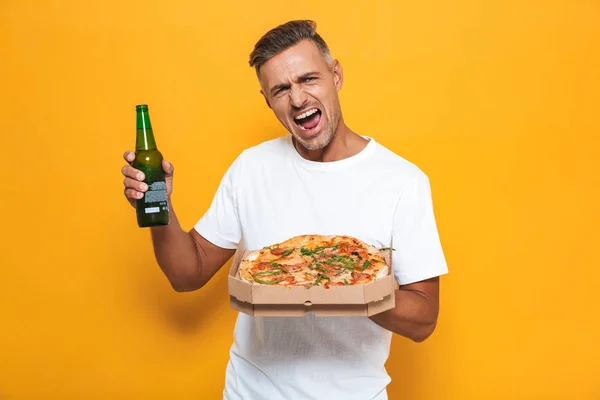 Imagen del hombre excitado 30s en camiseta blanca bebiendo cerveza y eati — Foto de Stock