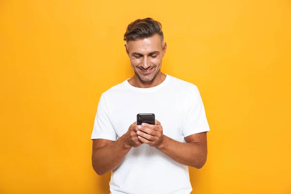 Šťastný muž představuje izolované žlutá stěna pozadí pomocí mobilního telefonu. — Stock fotografie