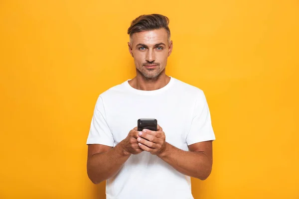 Bonito homem posando isolado sobre fundo da parede amarela usando telefone celular . — Fotografia de Stock