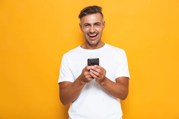 Ευτυχισμένος άνθρωπος θέτοντας απομονωμένες φόντο κίτρινο τοίχο χρησιμοποιώντας κινητό τηλέφωνο. — Φωτογραφία Αρχείου