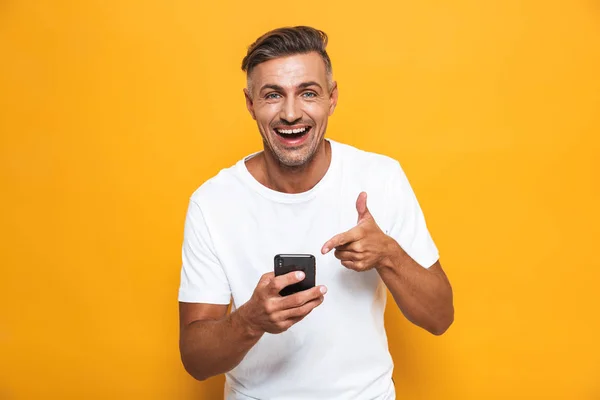 Ευτυχισμένος άνθρωπος θέτοντας απομονωμένες φόντο κίτρινο τοίχο χρησιμοποιώντας κινητό τηλέφωνο. — Φωτογραφία Αρχείου