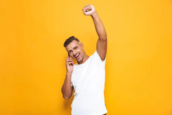 Homem emocional posando isolado sobre fundo de parede amarela falando por telefone celular . — Fotografia de Stock