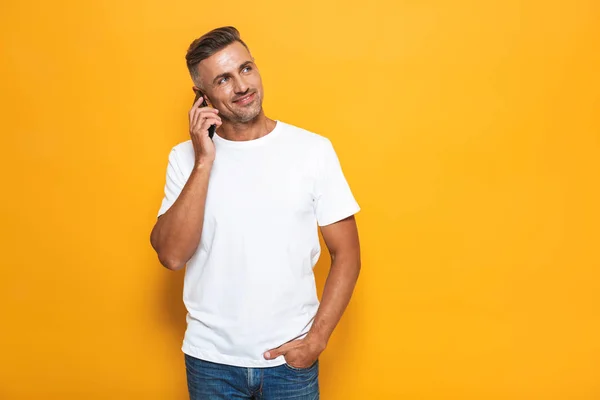 Homem emocional posando isolado sobre fundo de parede amarela falando por telefone celular . — Fotografia de Stock