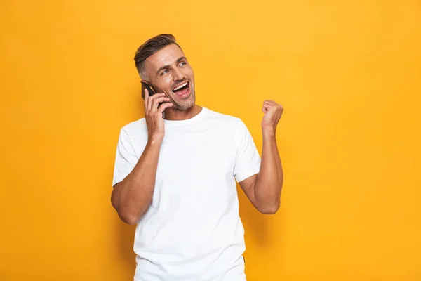 Homem emocional posando isolado sobre fundo de parede amarela falando por telefone celular . — Fotografia de Stock