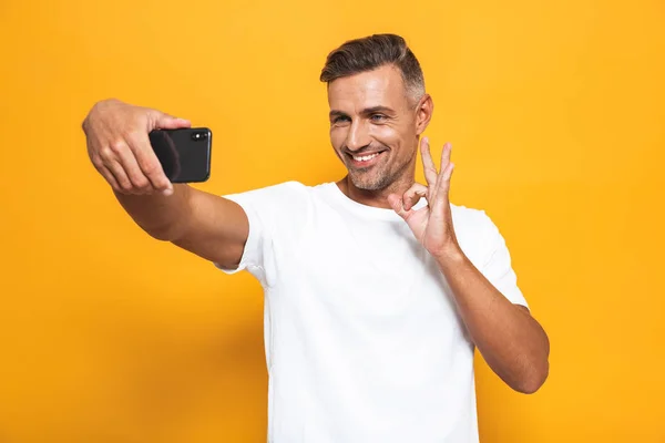 Imagen del joven de 30 años en camiseta blanca sonriendo y tomando selfi — Foto de Stock