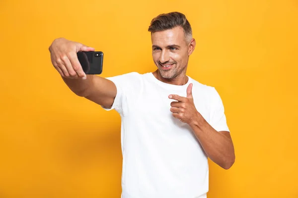 Imagen del hombre feliz de 30 años en camiseta blanca sonriendo y tomando selfi — Foto de Stock