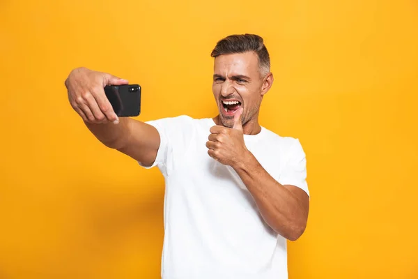 Imagen del hombre moreno de 30 años en camiseta blanca sonriendo y tomando se — Foto de Stock