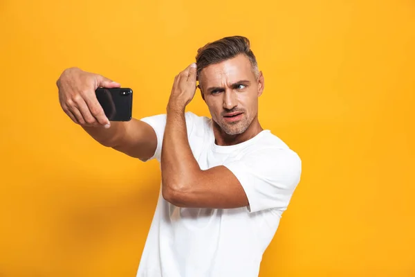 Imagen de hombre guapo de 30 años en camiseta blanca haciendo gestos y tomando — Foto de Stock