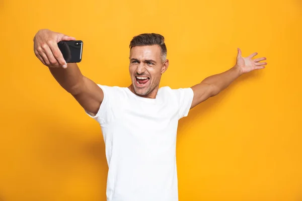 Imagen del hombre alegre de 30 años en camiseta blanca haciendo gestos y tomando se — Foto de Stock