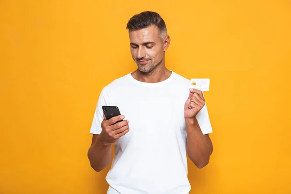 Bilden av Europeiska kille 30s i vit t-shirt innehav mobiltelefon — Stockfoto