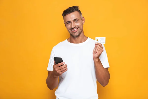 Image of cheerful guy 30s in white t-shirt holding mobile phone — Stock Photo, Image