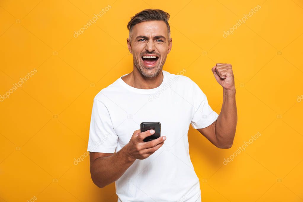 Happy man posing isolated over yellow wall background using mobile phone.