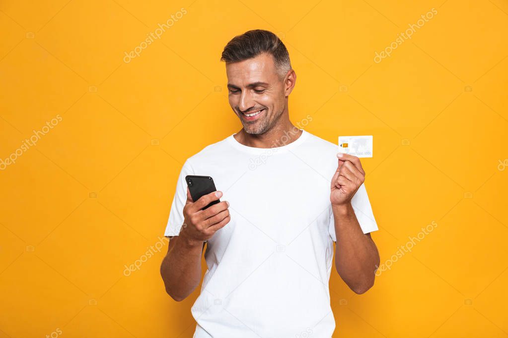 Image of beautiful guy 30s in white t-shirt holding mobile phone