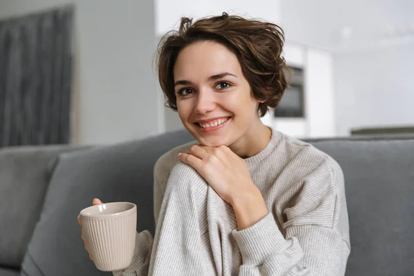 Šťastná mladá žena seděla doma na gauči — Stock fotografie