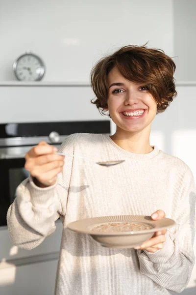 Glimlachende hongerige jonge vrouw staande op de koelkast — Stockfoto