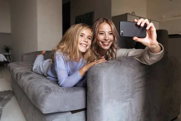 Jovem feliz com sua irmãzinha dentro de casa tirar uma selfie por telefone celular . — Fotografia de Stock