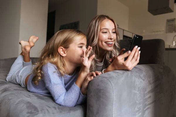 Glückliche junge Frau mit ihrer kleinen Schwester zu Hause mit dem Handy. — Stockfoto