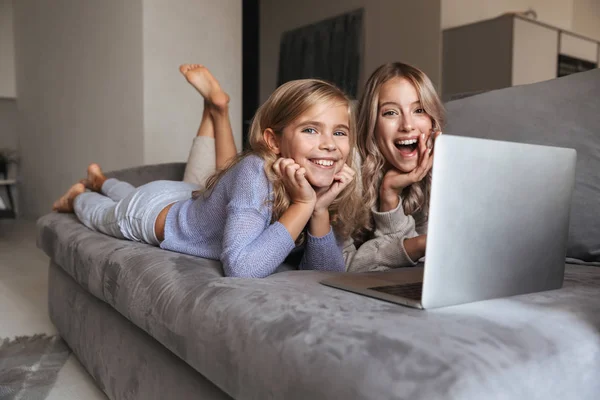 Jonge vrouw met haar kleine zusje binnenshuis thuis met behulp van laptopcomputer. — Stockfoto