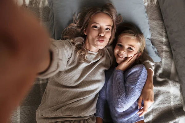 Feliz joven mujer con su hermana pequeña en el interior en casa tomar una selfie por cámara . —  Fotos de Stock