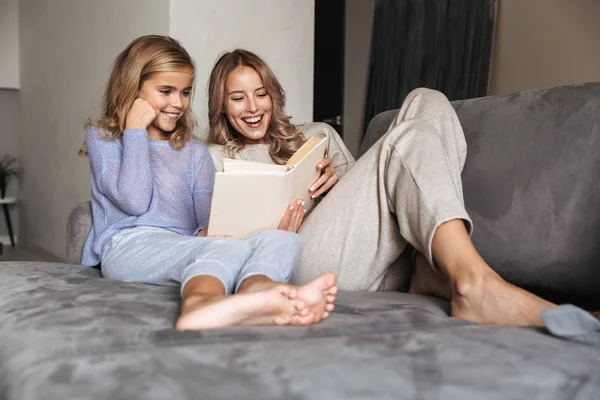 Jonge vrouw met haar kleine zusje binnenshuis thuis lezen boek. — Stockfoto