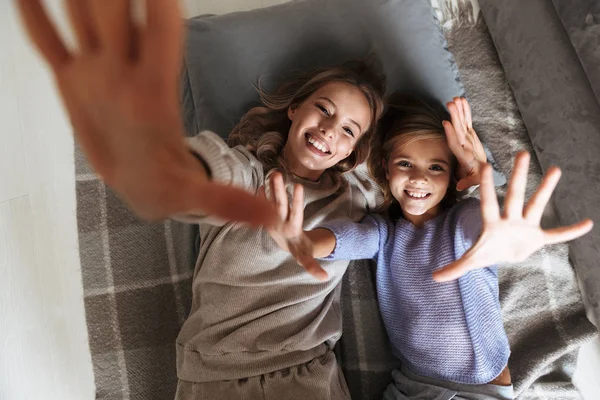 Feliz joven mujer con su hermana pequeña en el interior en casa poner las manos arriba . —  Fotos de Stock