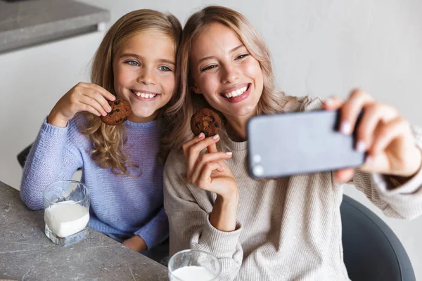 Glückliche Mädchen Schwestern in der Küche drinnen essen ein gemeinsames Frühstück machen ein Selfie mit dem Telefon. — Stockfoto