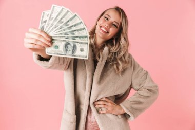 Young pretty woman posing isolated over pink wall background holding money. clipart