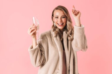 Duygusal genç güzel kadın üzerinde pembe duvar arka plan cam alkol içki ile tutarak izole poz.