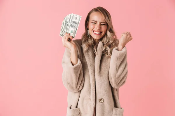 Fiatal, csinos nő pózol elszigetelt, felett tartja a pénzt rózsaszín háttér. — Stock Fotó