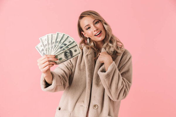 Молодая красивая женщина позирует изолированно на розовом фоне стены держа деньги
.