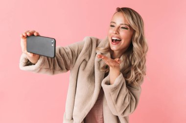 Genç güzel kadın pembe duvar arka plan üzerinde izole poz almak bir selfie cep telefonuyla.