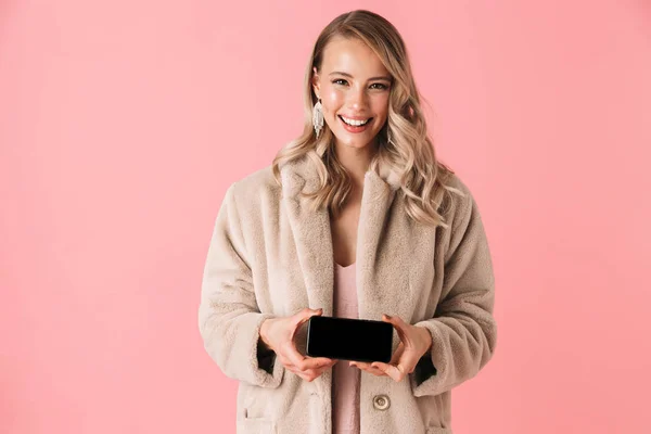 Όμορφη happy νεαρή γυναίκα όμορφη θέτοντας απομονωμένες φόντο ροζ τοίχο, δείχνοντας την οθόνη του κινητού τηλεφώνου. — Φωτογραφία Αρχείου